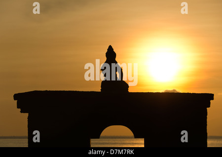 Silhouette di Budda seduto su arch contro il sorgere del sole e cielo arancione Foto Stock