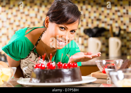 Donna asiatica presentando in casa torta al cioccolato con ciliegie ha infornato nella sua cucina per dessert Foto Stock