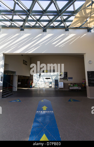 L'entrata con tetto di vetro al museo della bomba atomica di Nagasaki con frecce direzionali blu che puntano sul pavimento al banco dei biglietti. Foto Stock