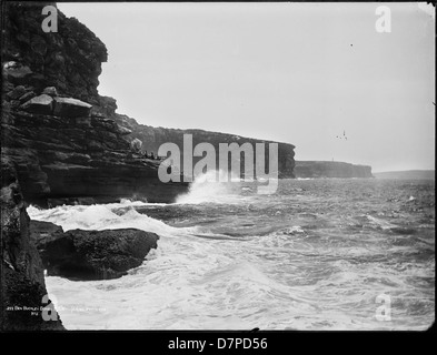 Questa fotografia in bianco e nero cattura il paesaggio spettacolare di Ben Buckler, Bondi, New South Wales, con le scogliere aspre e le onde che si infrangono. L'immagine mostra le potenti forze della natura lungo la costa australiana. Foto Stock