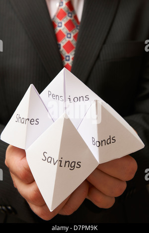 Business man tenendo la carta origami fortune teller con risparmi,obbligazioni, azioni e le pensioni scritto su di esso Foto Stock