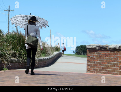 Donna che cammina con un ombrellone sulla Bondi a Coogee a piedi in Australia Foto Stock