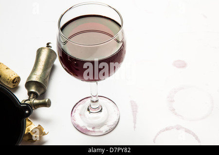 Un bicchiere pieno di vino rosso con involucro, sughero, e cavatappi con ghiera di vino le macchie dal vetro. Foto Stock