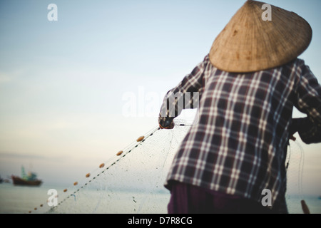 Un pescatore casting net presso la spiaggia di Mui Ne, Vietnam Foto Stock