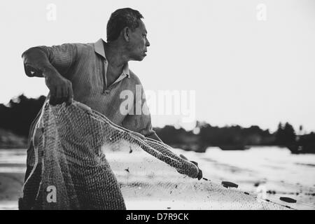 Un pescatore casting net presso la spiaggia di Mui Ne, Vietnam Foto Stock