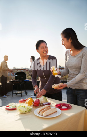 Madre e figlia la preparazione di hot dog per barbeque, padre e figlio di preparare le salsicce sul barbecue Foto Stock