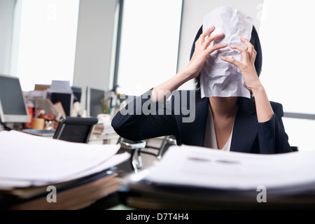 Giovane imprenditrice seduto alla scrivania che copre il volto con un foglio di carta Foto Stock