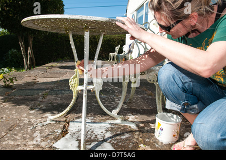 Una donna lava e pulisce bianco patio giardino mobili su una soleggiata giornata di primavera pronto per l'estate i pasti al fresco Foto Stock