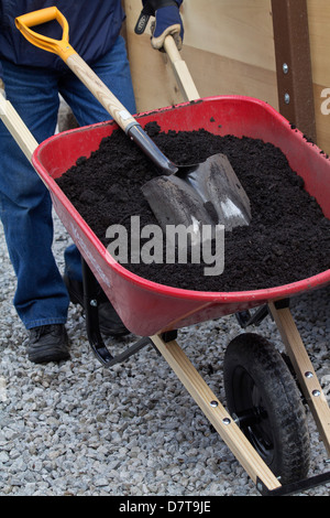 Lavori primaverili in giardino un uomo spinge il carpino ruota con un terreno pieno e una pala in alto dalle immagini dall'alto in verticale negli Stati Uniti ad alta risoluzione Foto Stock