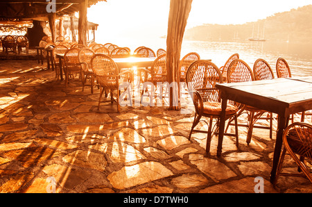 Seaside Cafe in arancio brillante luce del tramonto, grazioso bar con sedie in legno e tabelle sulla riva del mare, resort di lusso, vacanze estive Foto Stock