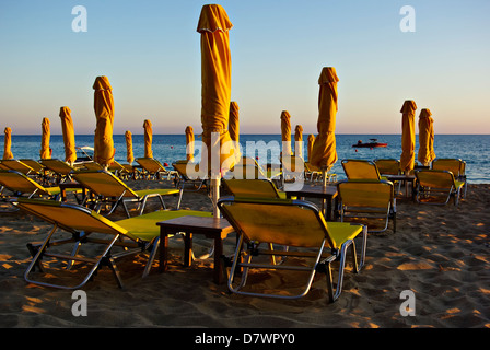 Il giallo di ombrelloni e lettini in spiaggia sabbiosa a estate tramonto con il blu del mare e del cielo in background. Foto Stock