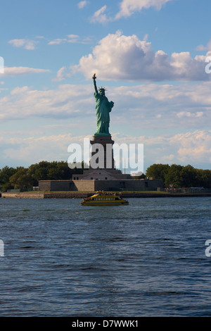 La Statua della Libertà su Liberty Island, New York, NY, STATI UNITI D'AMERICA, con un New York Water Taxi passando da di esso. Foto Stock