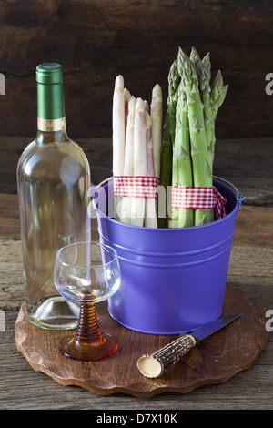 Bianco fresco e asparagi verdi in un secchio di metallo con una bottiglia di vino e un coltello su una tavola di legno Foto Stock