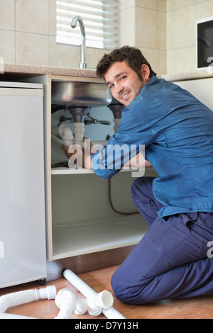 Plumber lavorando su tubi sotto il lavello da cucina Foto Stock