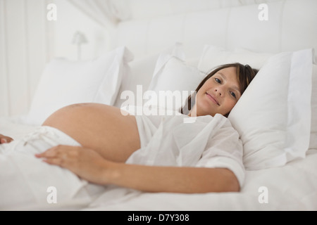 Donna incinta posa sul letto Foto Stock