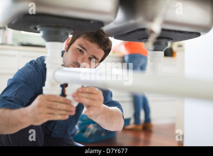 Plumber lavorando su tubi sotto il lavello Foto Stock