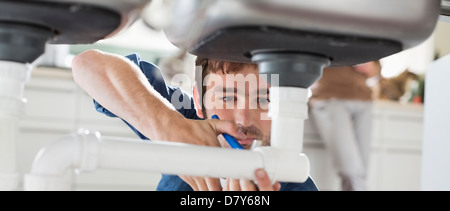 Plumber lavorando su tubi sotto il lavello Foto Stock