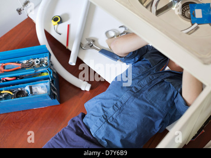 Plumber lavorando su tubi sotto il lavello Foto Stock