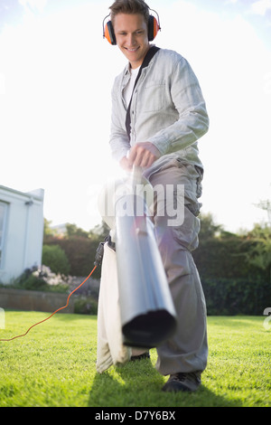 Uomo di foglie di soffiaggio in cortile Foto Stock