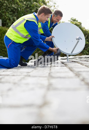 I lavoratori di installare una parabola satellitare sul tetto Foto Stock