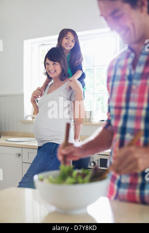 Gravidanza madre e figlia che guarda il padre condire insalate Foto Stock