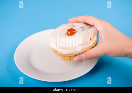 Mano femminile di prelevare un belga Bun off una piastra bianca contro uno sfondo blu. Foto Stock