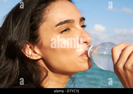 Donna ispanica di bere acqua in bottiglia sulla spiaggia Foto Stock