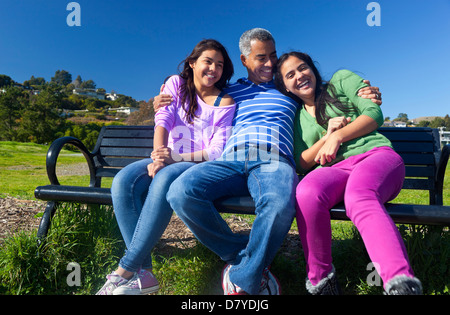 Padre ispanica e figlie seduto su una panchina nel parco Foto Stock