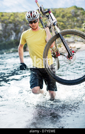 Uomo che porta in mountain bike nel fiume Foto Stock
