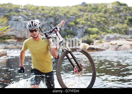 Uomo che porta in mountain bike nel fiume Foto Stock