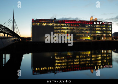 La sede centrale illuminata della BBC Scotland su Pacific Quay si riflette nel fiume Clyde al tramonto con il Ponte di Bell sulla sinistra, Glasgow, Scozia, Regno Unito Foto Stock