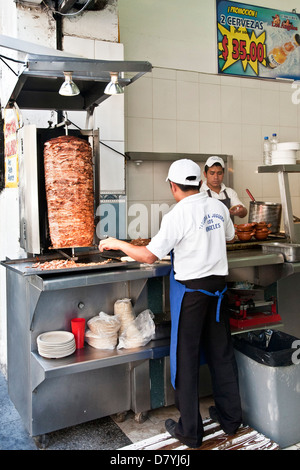 2 giovani messicani, uomini lavoratori in acciaio inossidabile contatore in un ristorante fast food fare tacos al pastore da carni di tostatura su spit Foto Stock