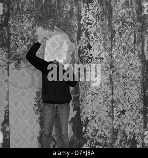 L'uomo con un pezzo di carta da parati strappata in camera decaduto. In bianco e nero. Foto Stock