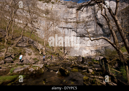 Sunny View delle persone che camminano da beck al piede di Malham Cove - enorme, drammatico, curvando roccia calcarea in splendide Yorkshire Dales, Inghilterra, GB, UK. Foto Stock