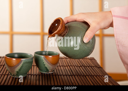 Mano femmina versando due tazze di sake Giapponese Foto Stock