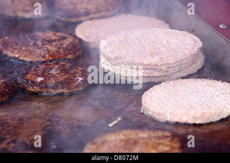 Crudi e cotti hamburger trasformati su un piano commerciale grill in corrispondenza di un evento esterno Foto Stock