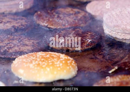 Crudi e cotti hamburger trasformati su un piano commerciale grill in corrispondenza di un evento esterno Foto Stock