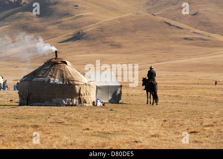 Uomo del Kirghizistan in sella ad un cavallo nero si avvicina ad una yurt in highland pascoli presso la canzone Kul lago. Regione di Naryn, Kirghizistan Foto Stock