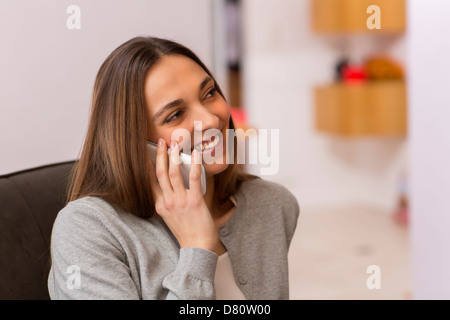 Bella femmina utilizzando il bianco telefono cellulare a casa a parlare con gli amici Foto Stock