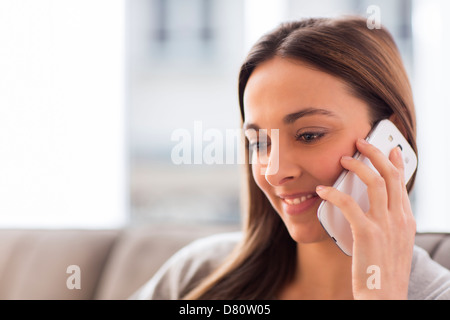 Piuttosto giovane donna utilizzando il bianco telefono cellulare a casa Foto Stock