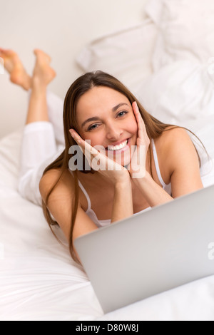 Attraente giovane donna in casa a lavorare sul computer portatile in camera da letto Foto Stock