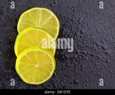 Freschi fette di lima con gocce d'acqua su ardesia nera sullo sfondo di pietra Foto Stock