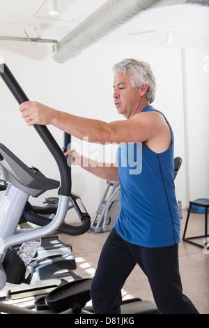 Vecchio uomo ispanico utilizzando macchina ellittica in palestra Foto Stock