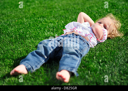 Carino bambina posa sull'erba verde nel parco Foto Stock