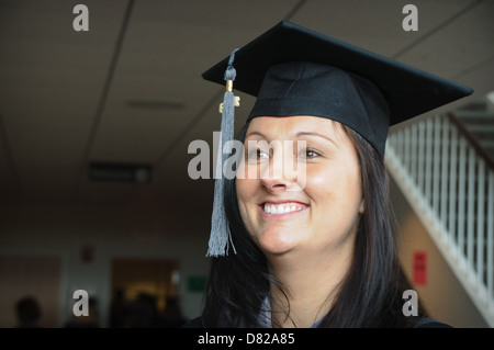 Giovane donna caucasica nel cappuccio e camice sorridendo dopo la laurea Foto Stock