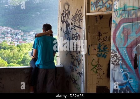 Giovane bacio al coperto di graffiti danneggiato guerra Stara Banka Staklena edificio in Mostar Bosnia Erzegovina Foto Stock