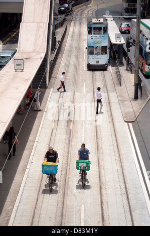 Consegna biciclette gli uomini a cavallo lungo i binari del tram nel Quartiere Wanchai dell'isola di Hong kong Foto Stock