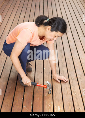 Foto verticale di donna matura schede di regolazione con il martello su un sbiadito naturale del legno di cedro deck Foto Stock