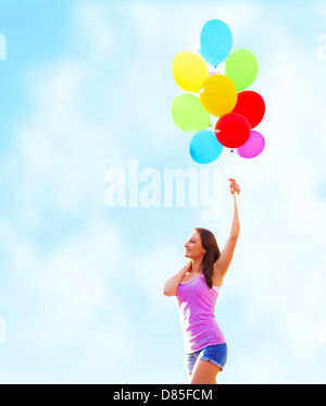 Bella giovane donna tenendo in mano molti palloncini colorati sul cielo azzurro sfondo, estate vacanze, concetto di divertimento Foto Stock