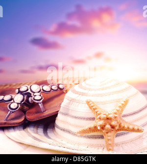 Closeup ancora la vita di spiaggia accessori su purpureo tramonto sfondo, flipflops e womens hat decorate con stelle marine Foto Stock